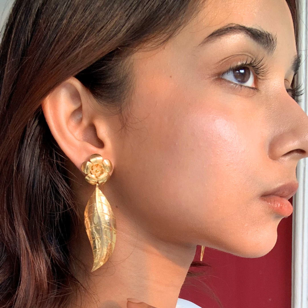Handcrafted gold-plated earring featuring a floral stud design with a detailed, dangling leaf motif, highlighting the earring’s shiny texture and elegant craftsmanship.