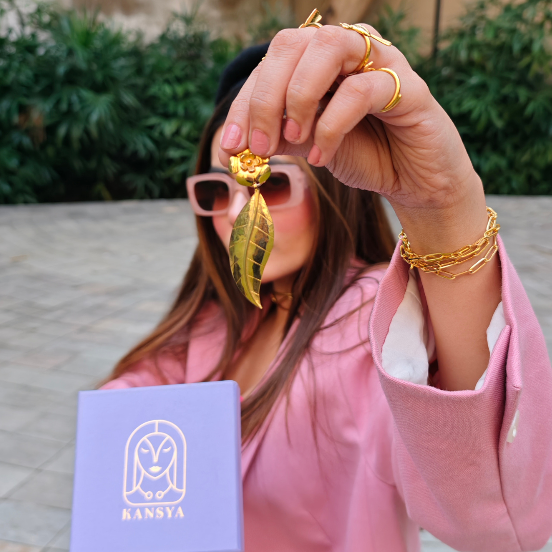 Handcrafted gold-plated earring featuring a floral stud design with a detailed, dangling leaf motif, highlighting the earring’s shiny texture and elegant craftsmanship.