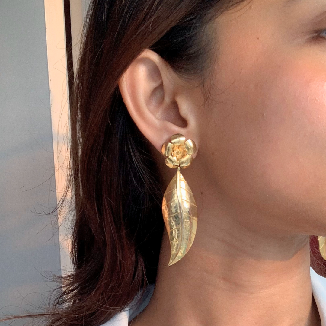 Handcrafted gold-plated earring featuring a floral stud design with a detailed, dangling leaf motif, highlighting the earring’s shiny texture and elegant craftsmanship.