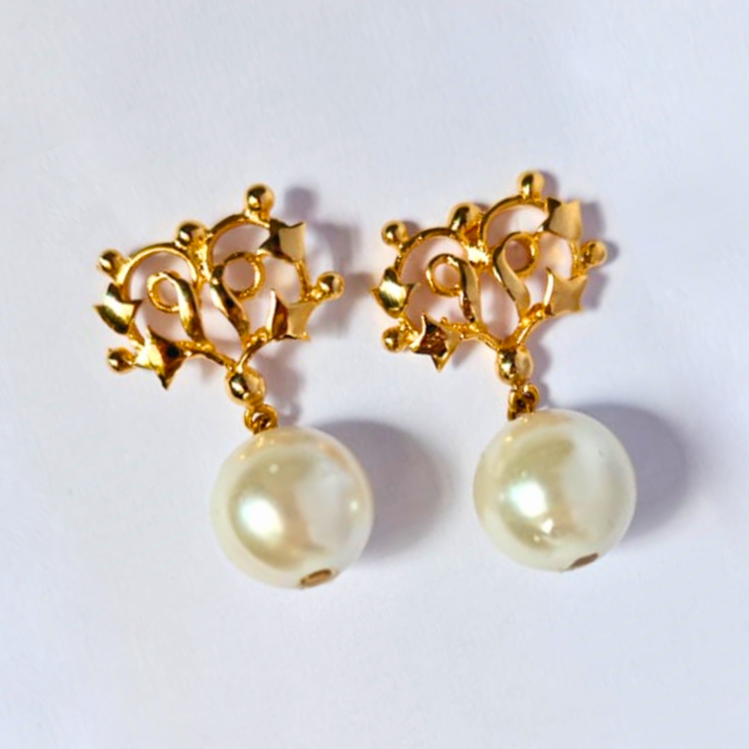 A pair of gold-plated earrings featuring intricate floral-inspired metalwork at the top and large round faux pearls dangling below