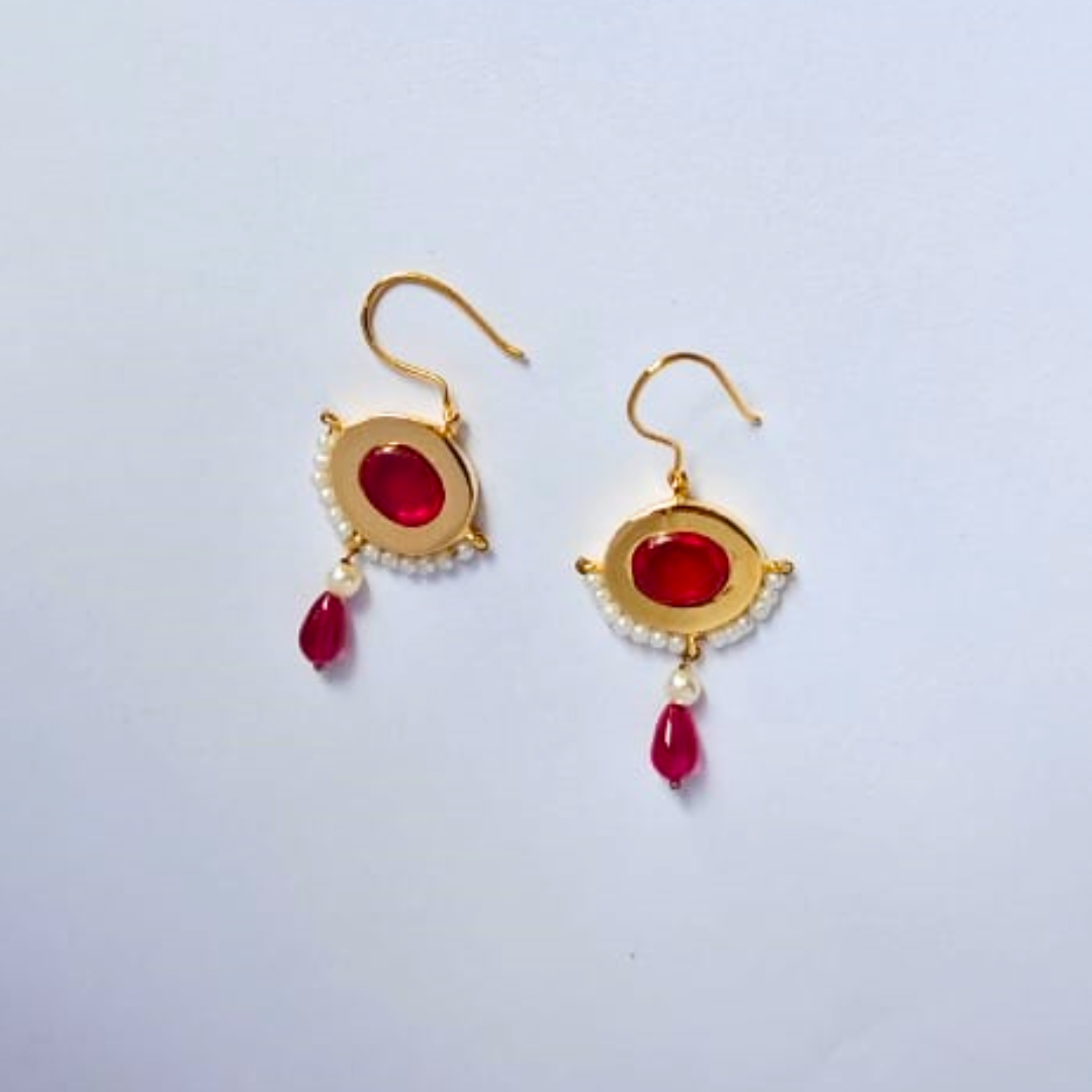 Pair of gold-plated drop earrings featuring bold red oval stones at the center, bordered with tiny white pearls and finished with red and pearl bead dangles