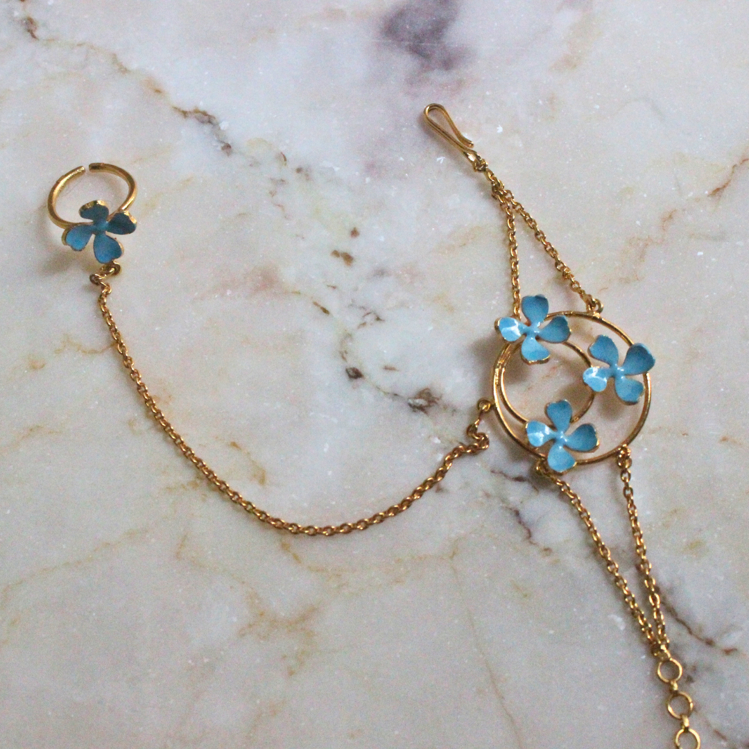 Handmade brass and 18k rhodium gold plated bracelet with fine chains connecting a circular floral motif of blue enamel flowers to a matching finger ring