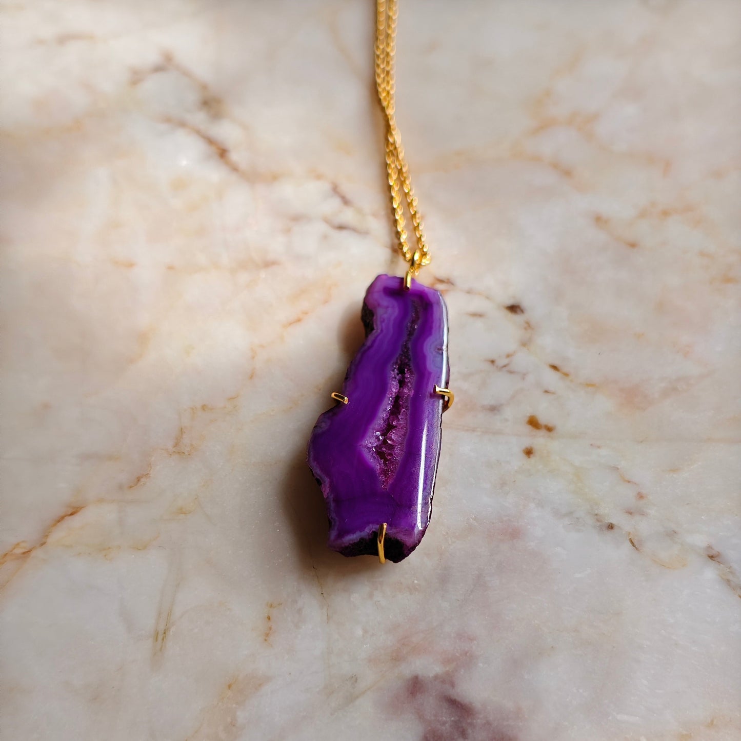 Purple geode pendant on a gold chain against a marble background