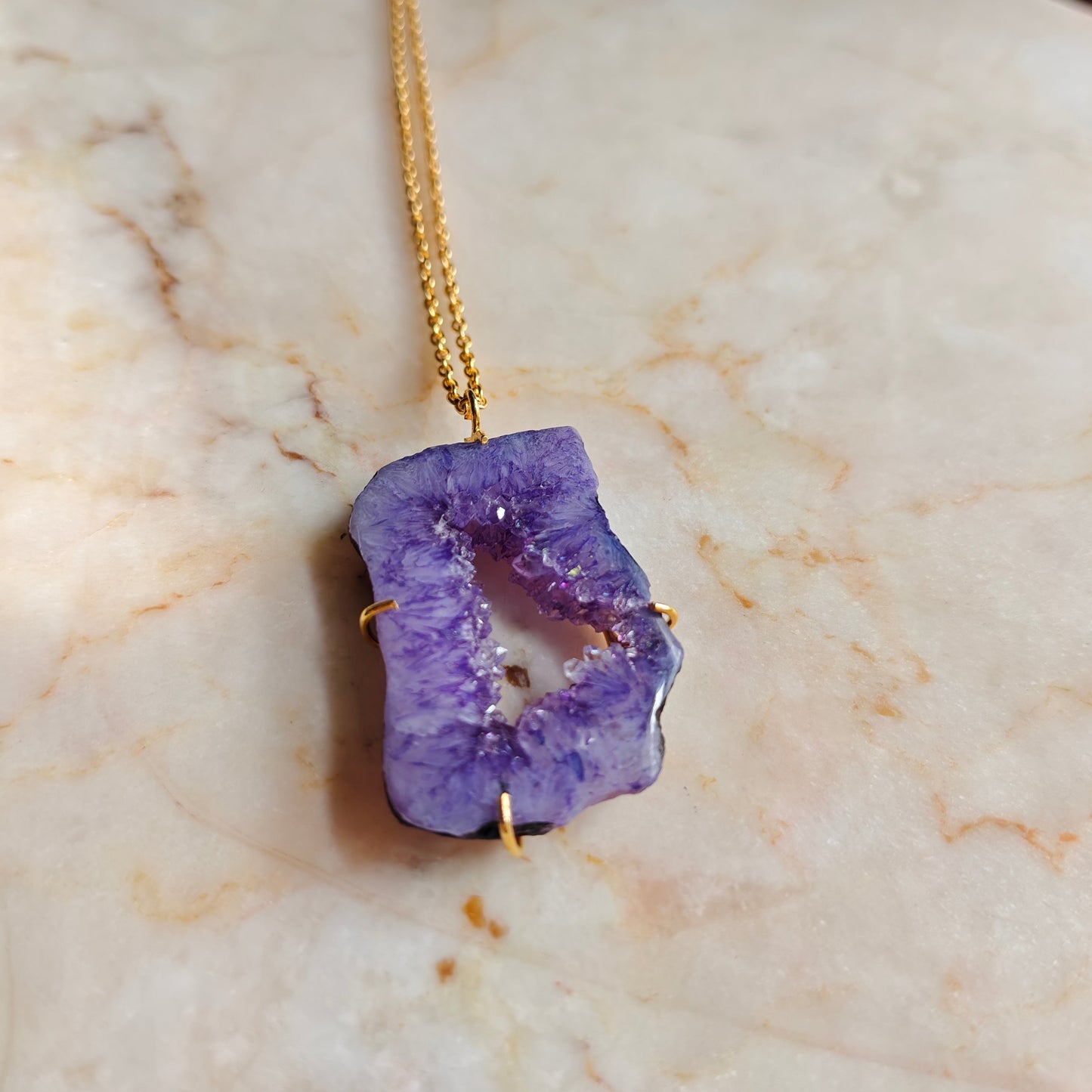 Purple geode necklace on a gold chain on a marble surface