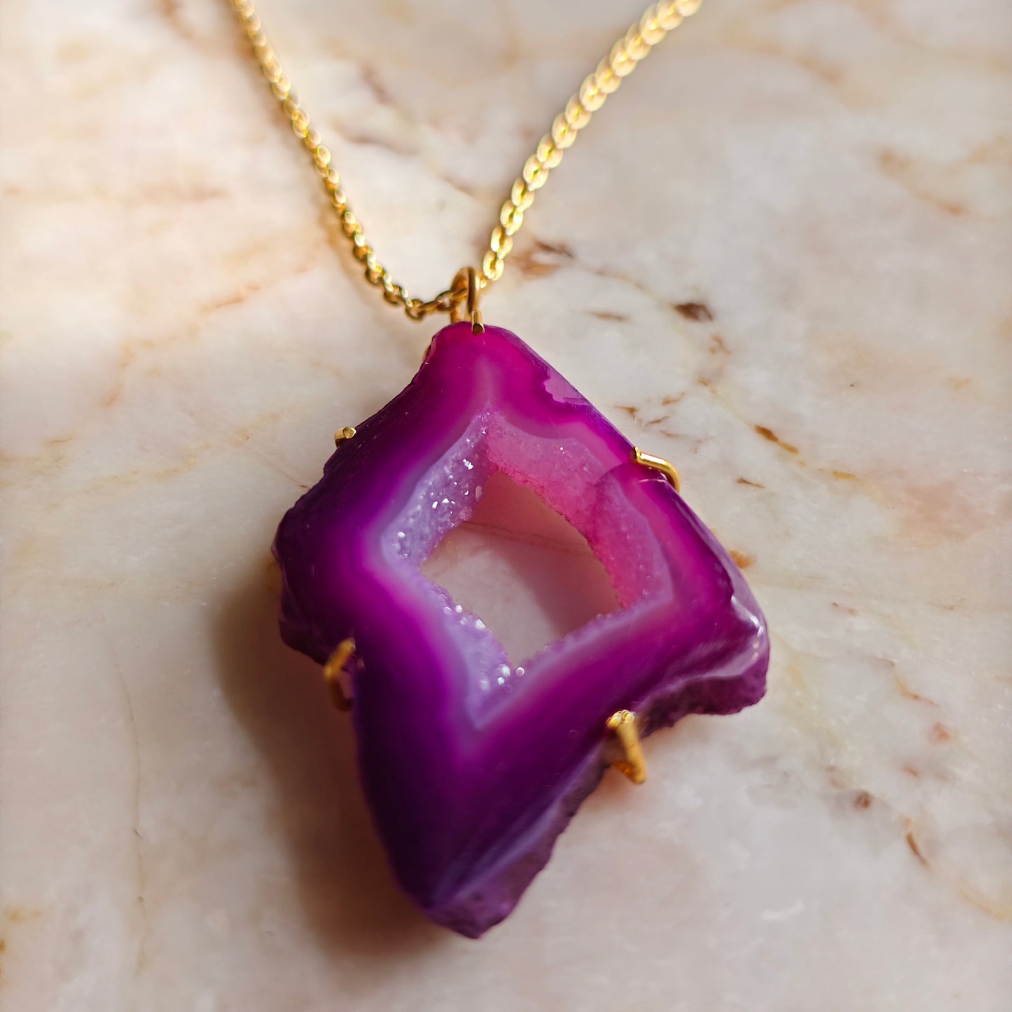 Purple agate pendant on a gold chain against a marble background