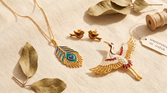 Peacock pendant, sparrow studs and crane brooch flat lay on cream linen – KANSYA Jewellery
