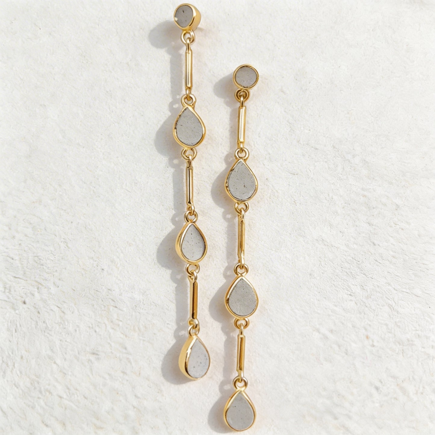 Gold and cement teardrop earrings on a textured white background