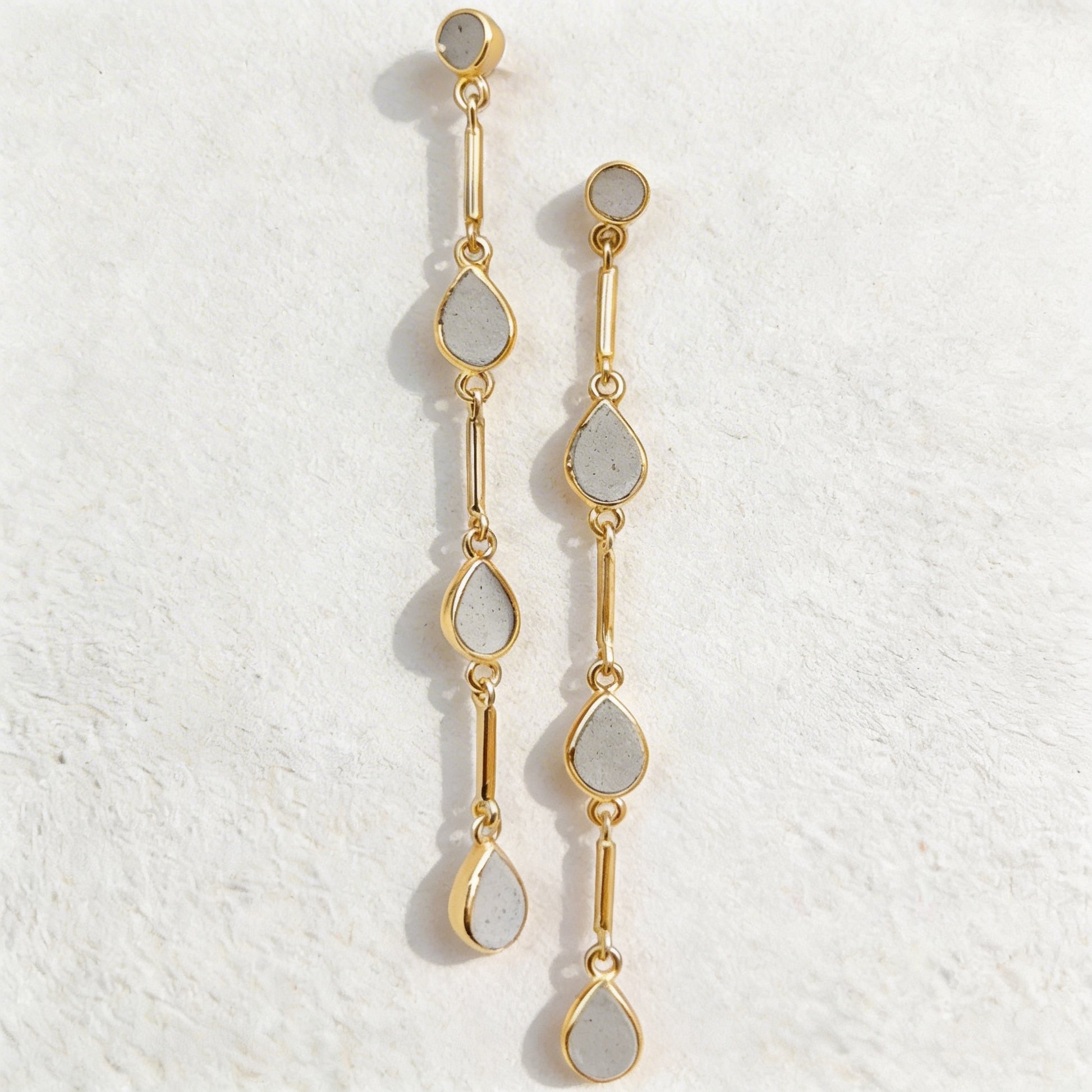 Gold and cement teardrop earrings on a textured white background