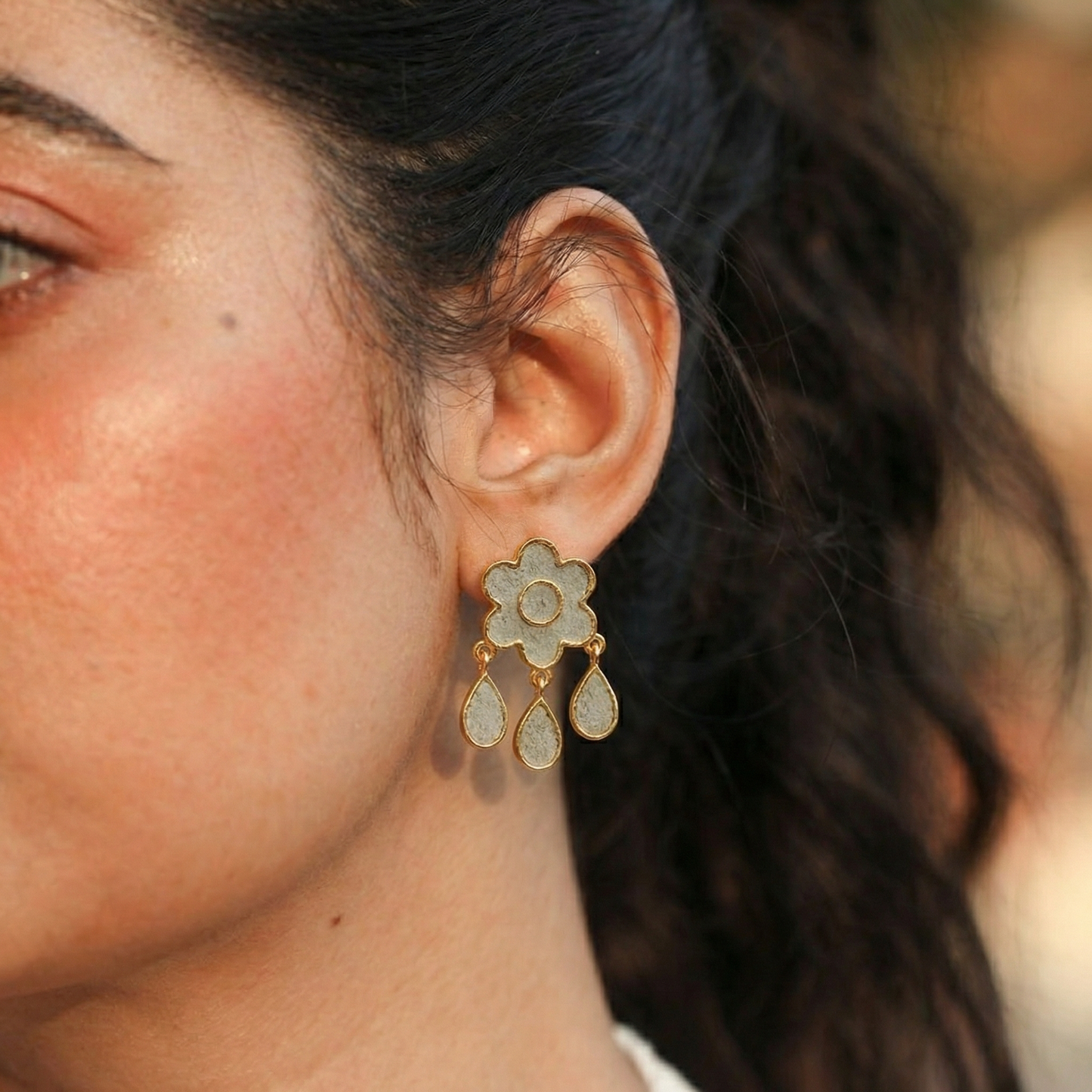 Close-up of a woman's ear wearing a gold and cement floral earring.