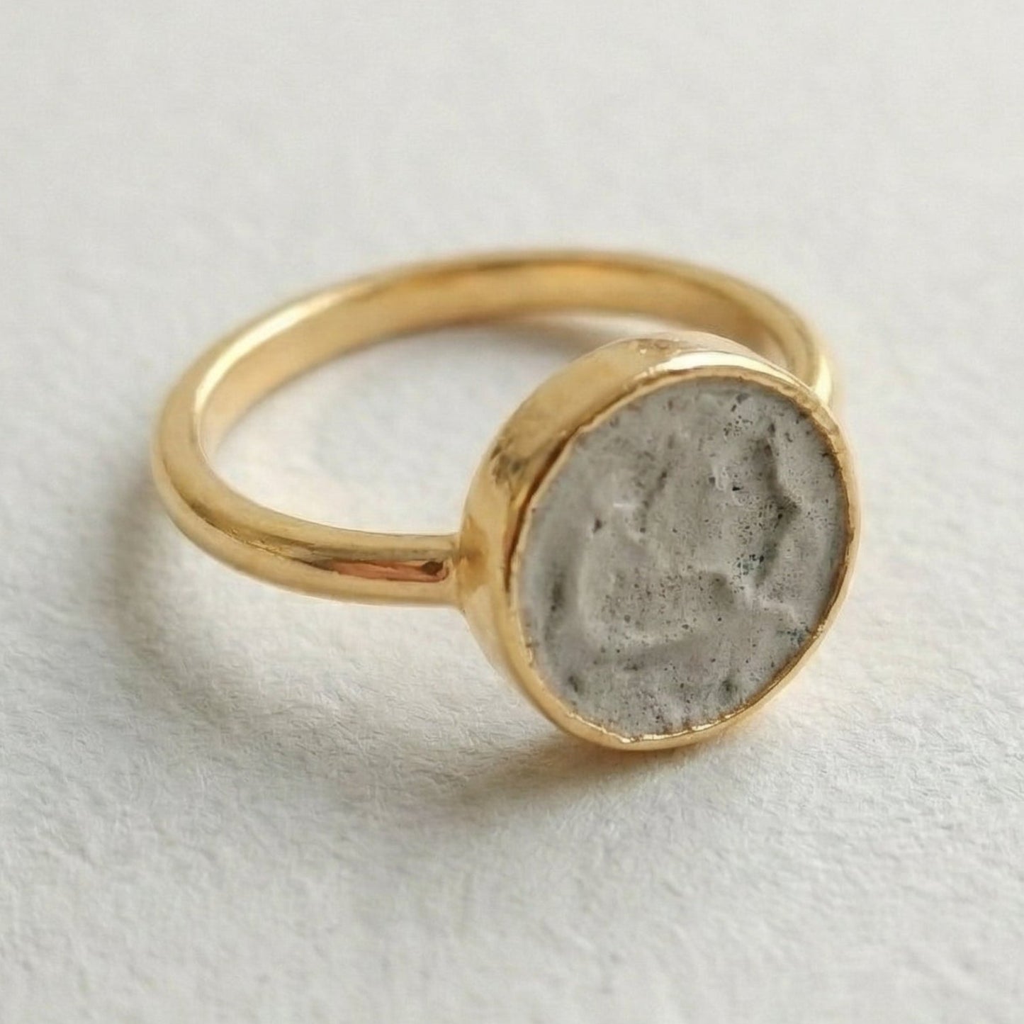Gold ring with a concrete-like stone on a light gray background