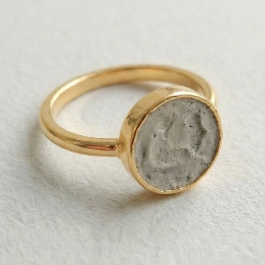 Gold ring with a concrete-like stone on a light gray background