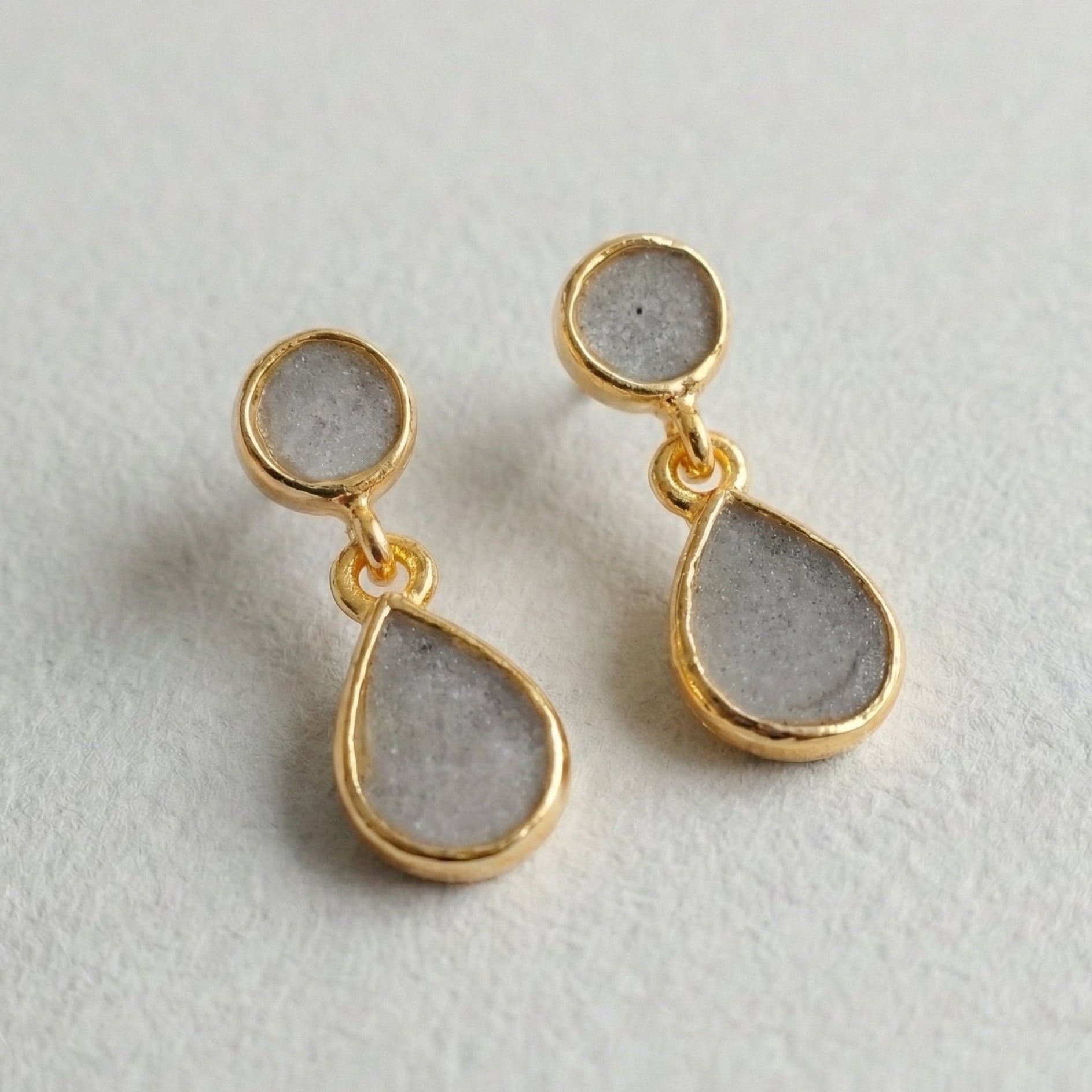 Gold and gray teardrop earrings on a light gray background