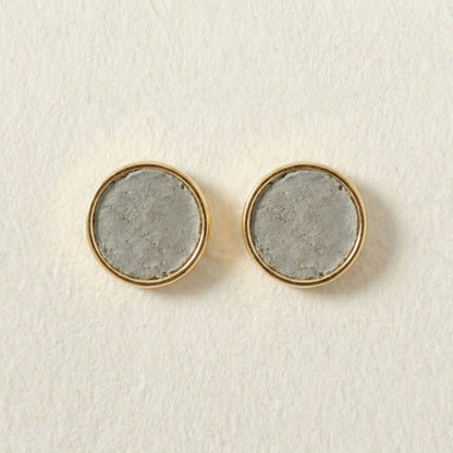 Round cement earrings with gold rims and concrete-like centers on a light beige background