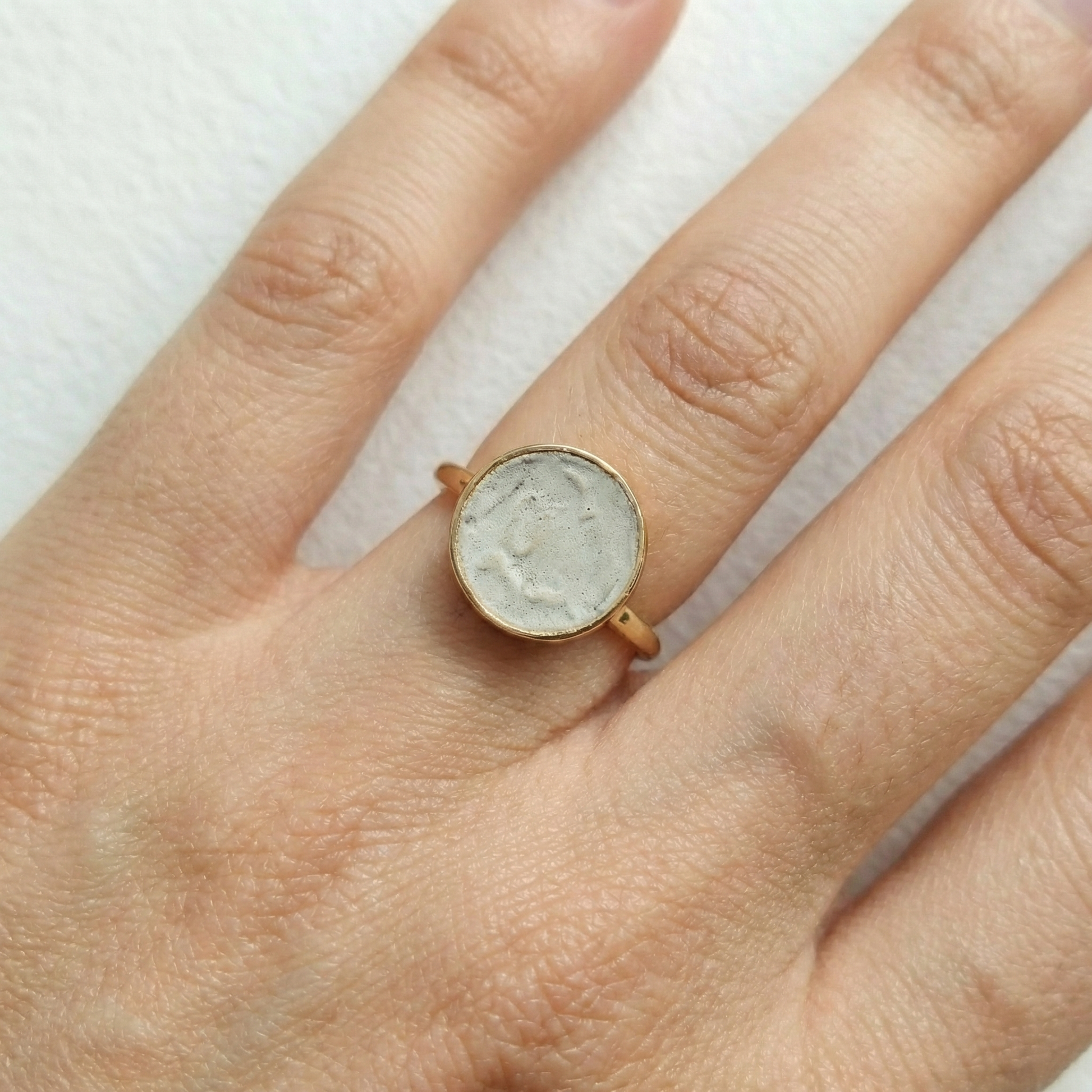 Gold ring with cement filled in on a person's finger against a white background