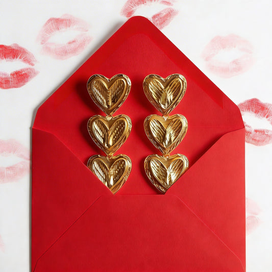 Gold heart-shaped earrings on a red envelope with lipstick patterned background