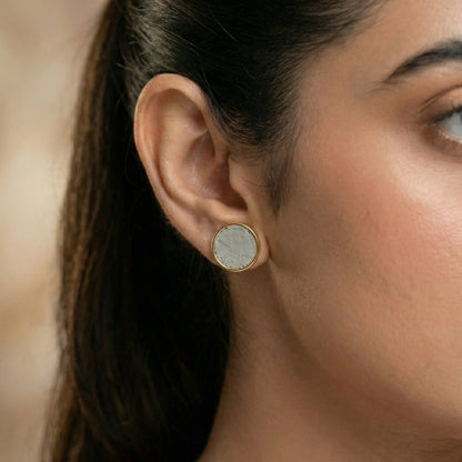 Close-up of a woman wearing gold cement filled earrings with a beige background
