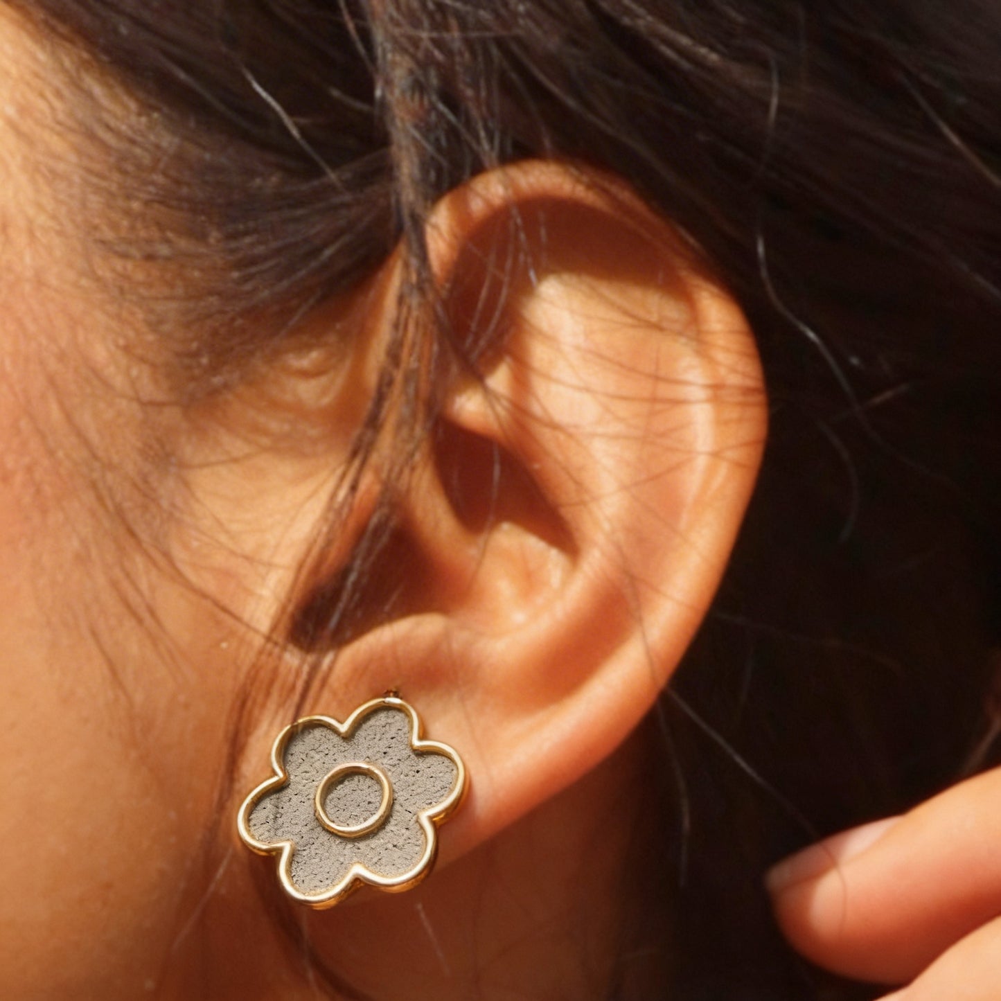 Close-up of an ear wearing a floral cement earring with a blurred background