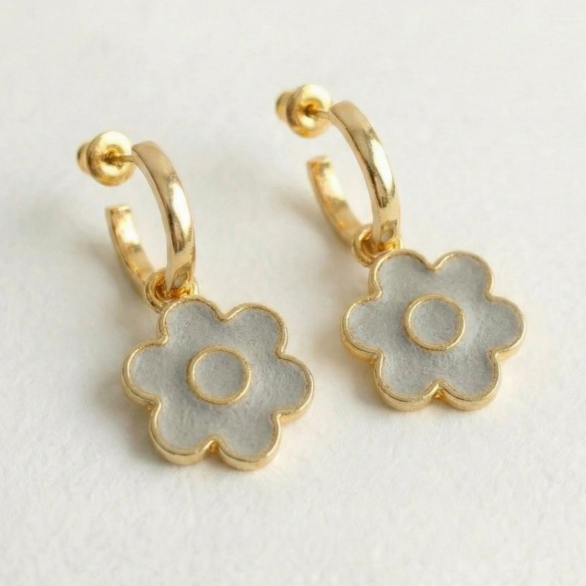 Detachable gold hoop earrings with flower-shaped cement charm on a light gray background