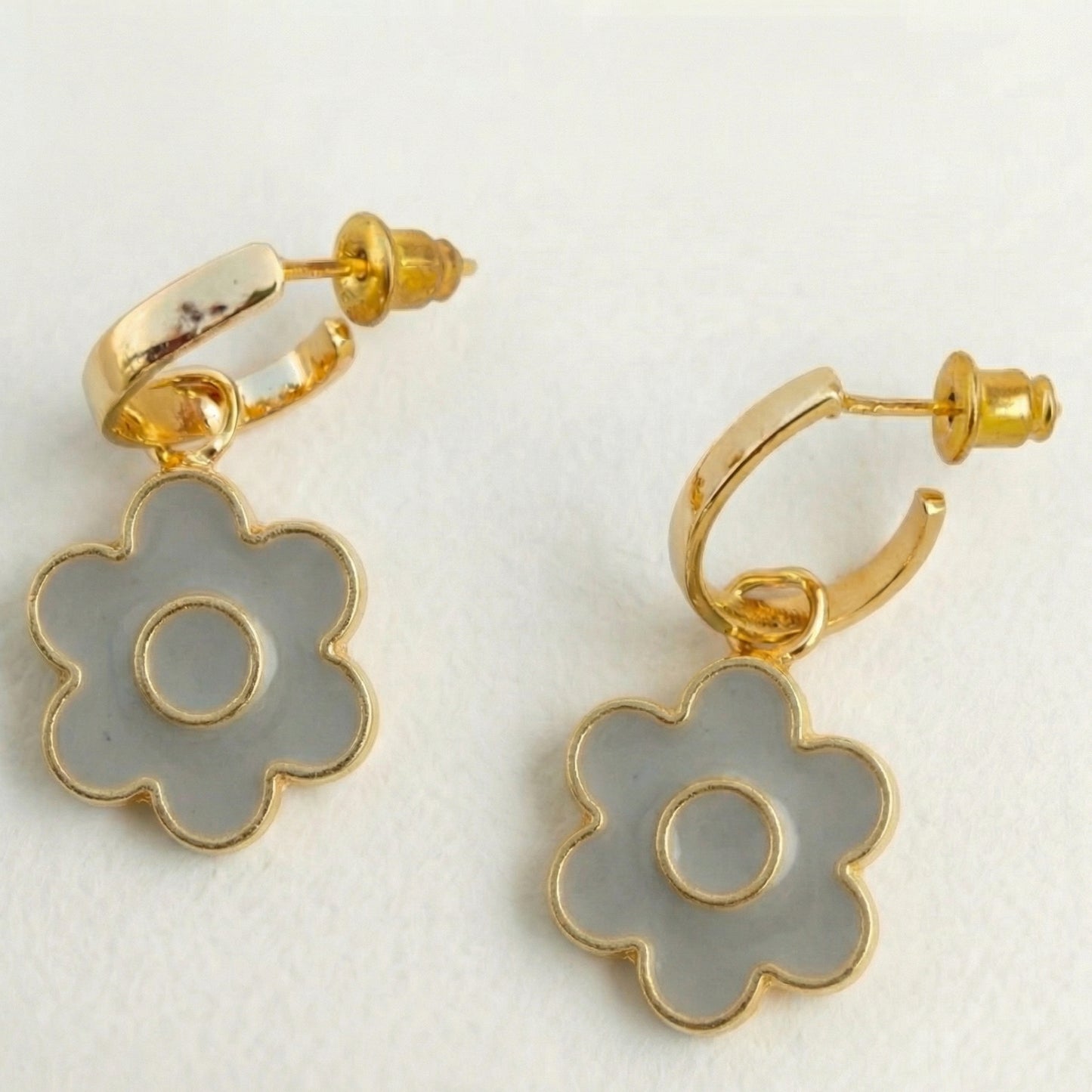 Gold hoop earrings with gray flower-shaped charms on a white background