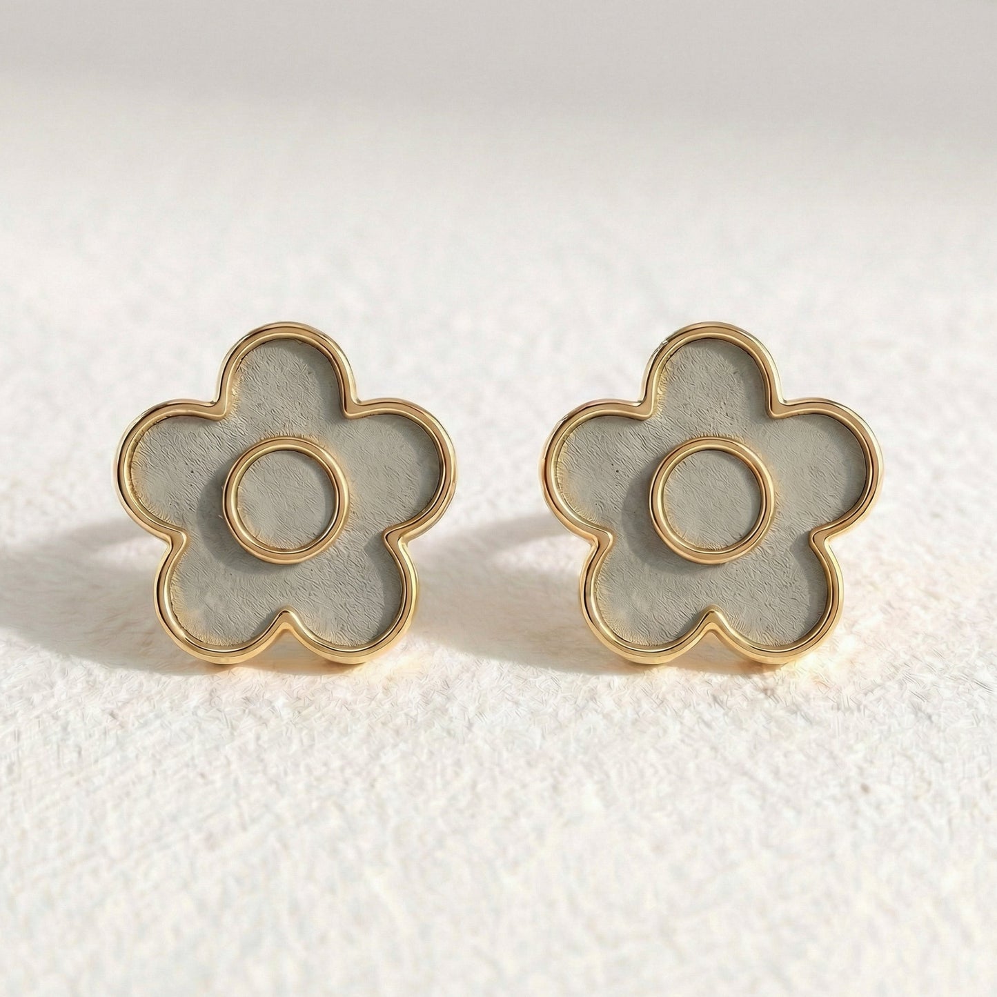 Flower-shaped earrings with gold frames on a textured white surface