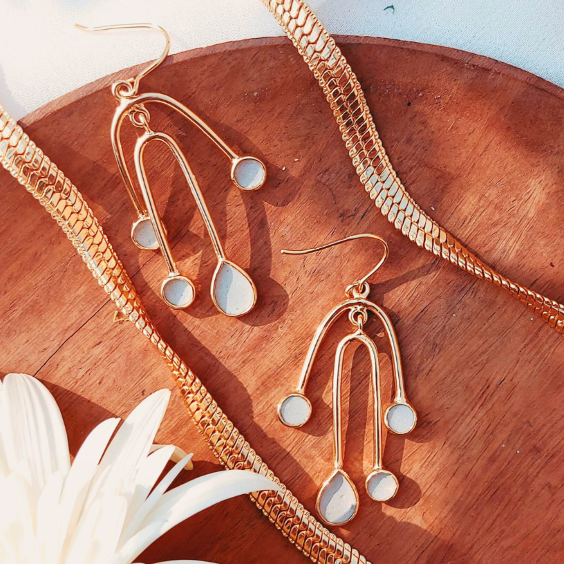 Gold earrings with cement filled drop and round shape on a wooden surface with a chain and flower.