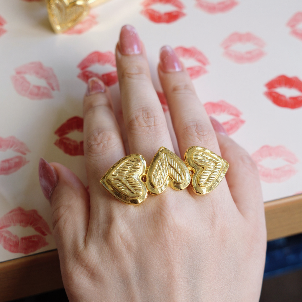 Hand wearing triple gold heart-shaped rings with a patterned background