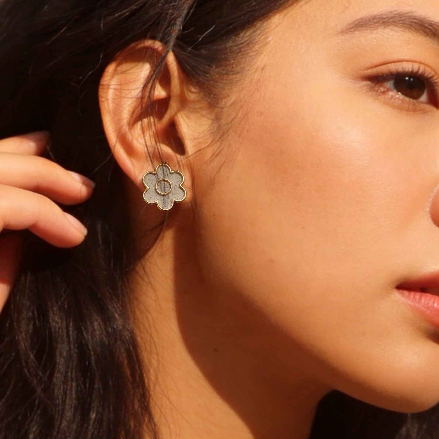 Close-up of a woman wearing a gold rhodium plated flower-shaped earring.