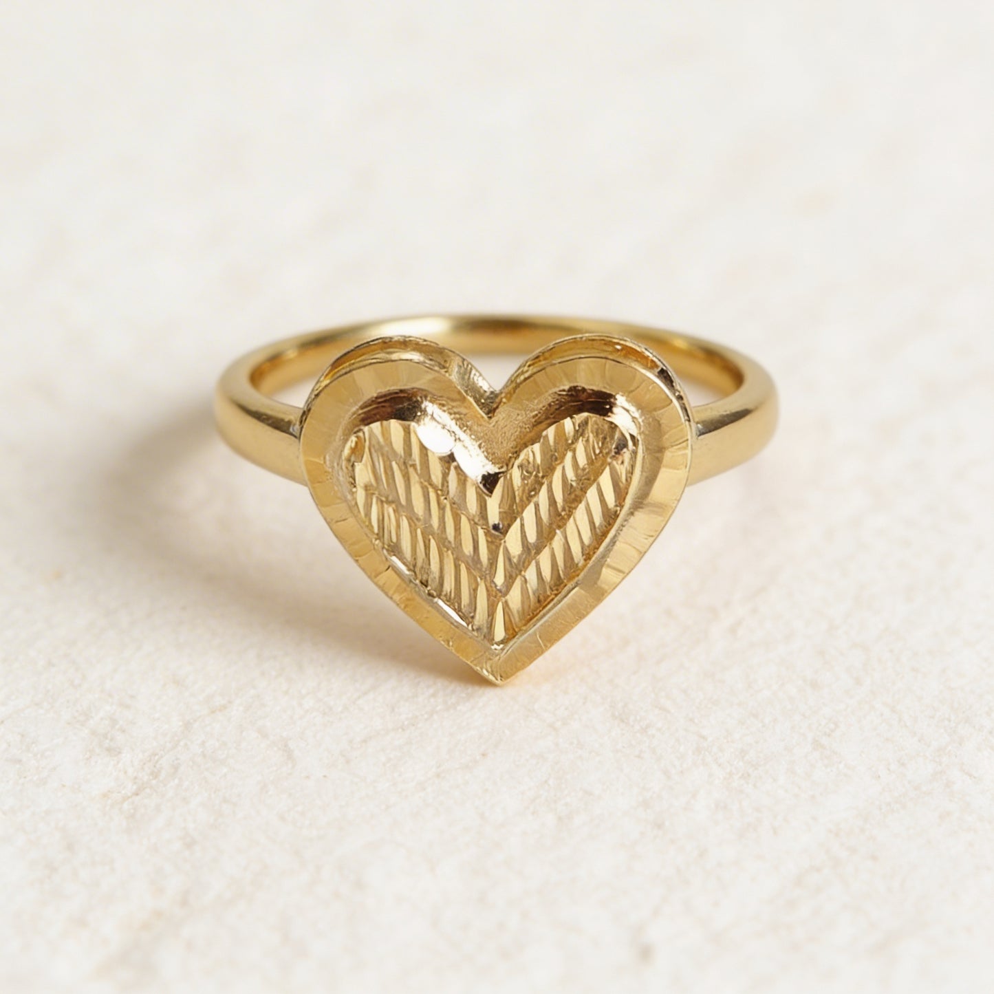 Gold heart-shaped ring on a textured beige background