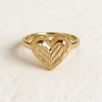 Gold heart-shaped ring on a textured beige background