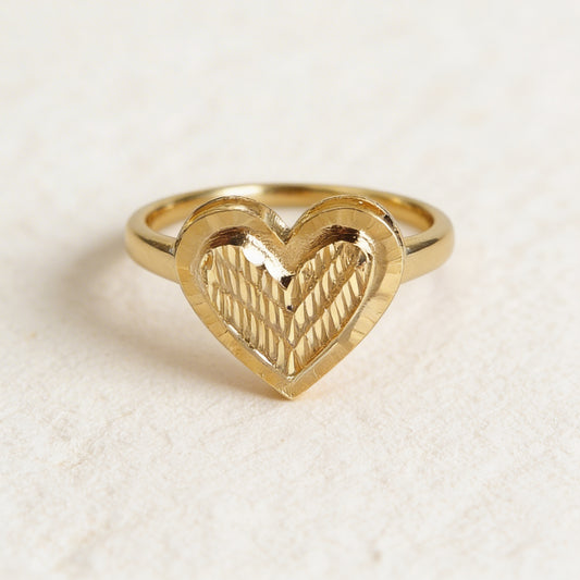 Gold heart-shaped ring on a textured beige background