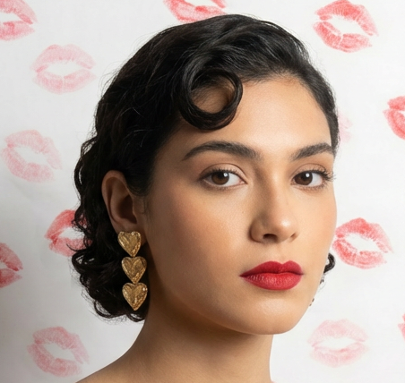 Woman wearing gold heart-shaped earrings with a pattern of pink lipstick marks in the background