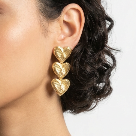 Gold heart-shaped earrings worn by a person with dark hair.