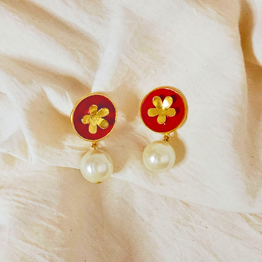A pair of handcrafted earrings featuring red Meena enamel discs with gold floral motifs and elegant faux pearl drops, set in 18K gold-plated brass.