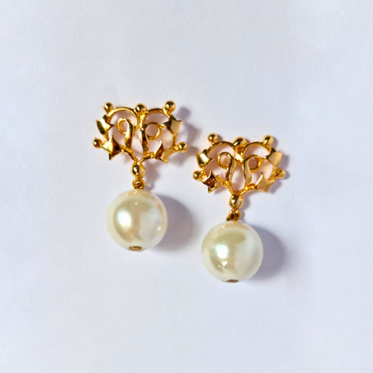 A pair of gold-plated earrings featuring intricate floral-inspired metalwork at the top and large round faux pearls dangling below