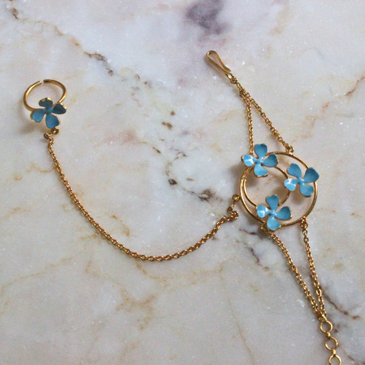 Handmade brass and 18k rhodium gold plated bracelet with fine chains connecting a circular floral motif of blue enamel flowers to a matching finger ring