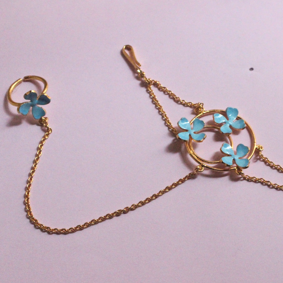 Handmade brass and 18k rhodium gold plated bracelet with fine chains connecting a circular floral motif of blue enamel flowers to a matching finger ring