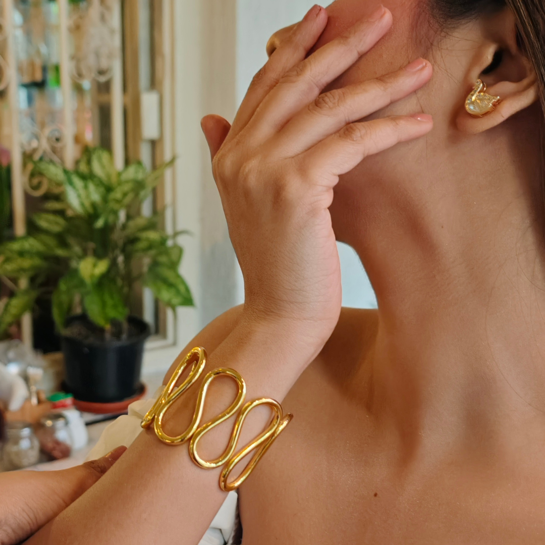 Gold-plated spiral handcuff bangle with wave-like design, crafted from brass