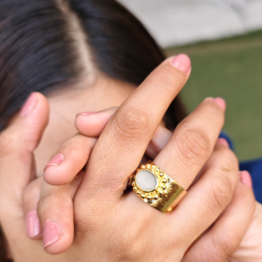 A bold Cement Halo Ring featuring a circular cement centerpiece framed by intricate golden detailing. The ring, made of brass and finished in 18K rhodium gold plating, exudes a blend of elegance and architectural edge