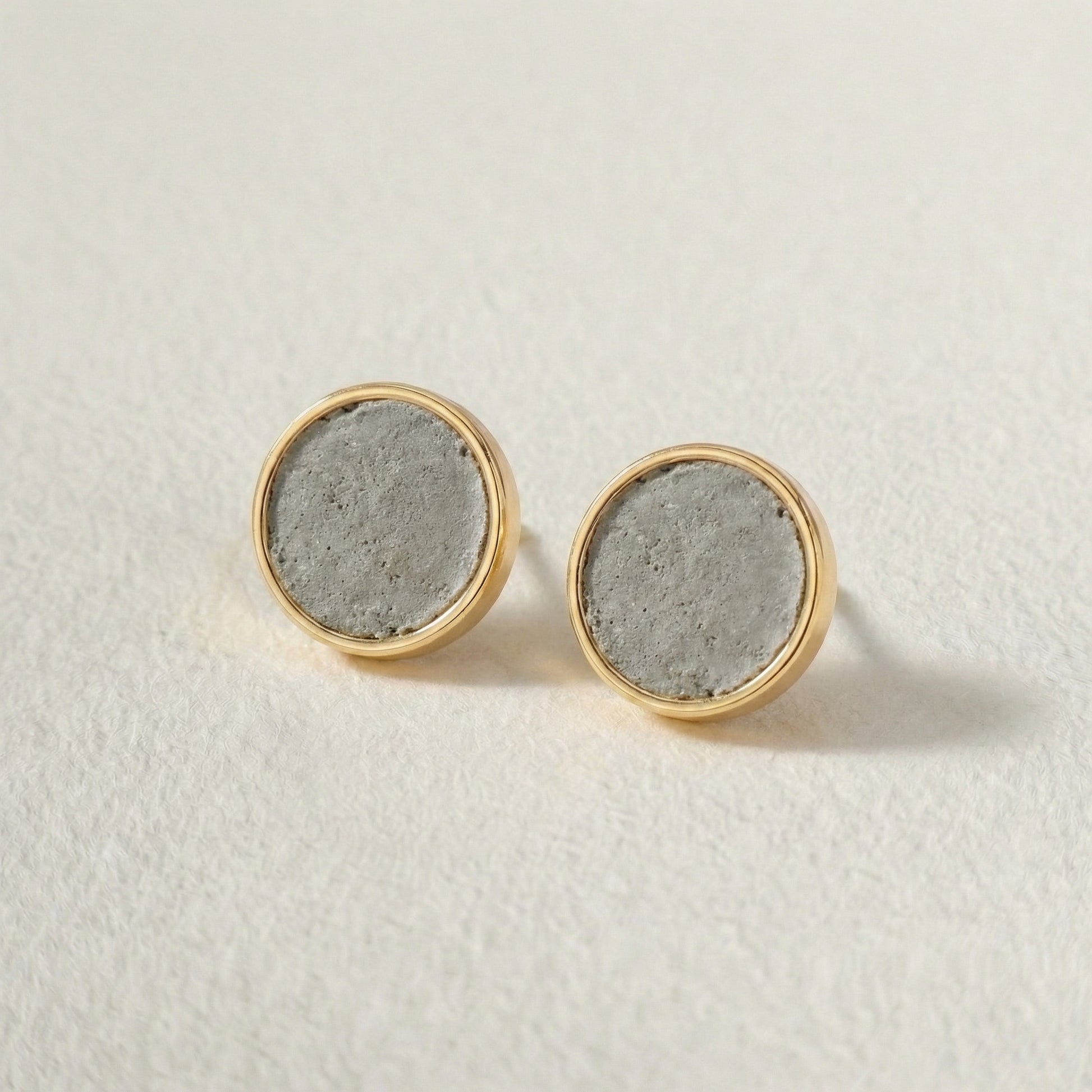 Pair of round earrings with gold rims and concrete-like centers on a light background