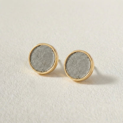 Pair of round earrings with gold rims and concrete-like centers on a light background