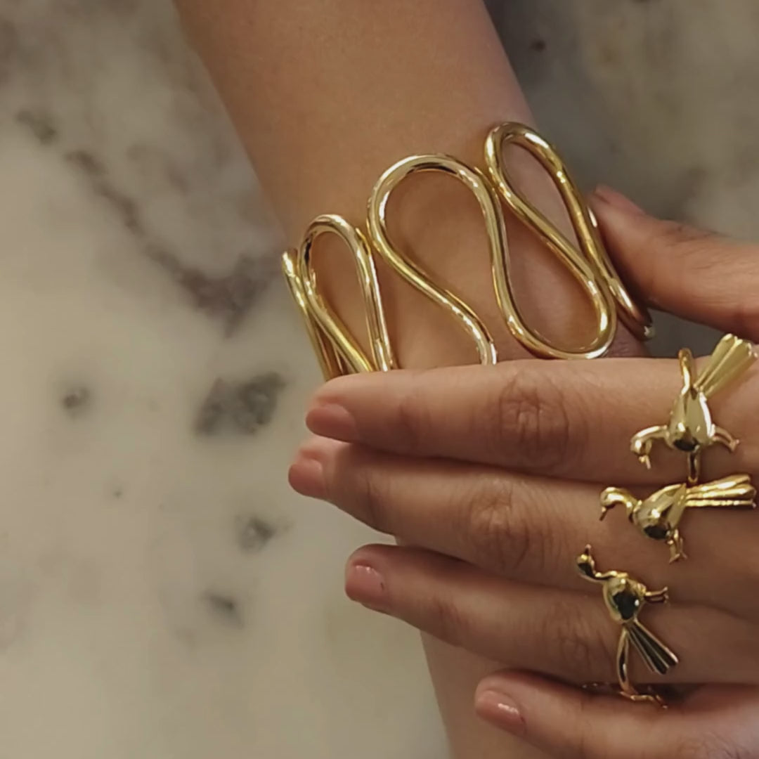 Gold-plated spiral handcuff bangle with wave-like design, crafted from brass
