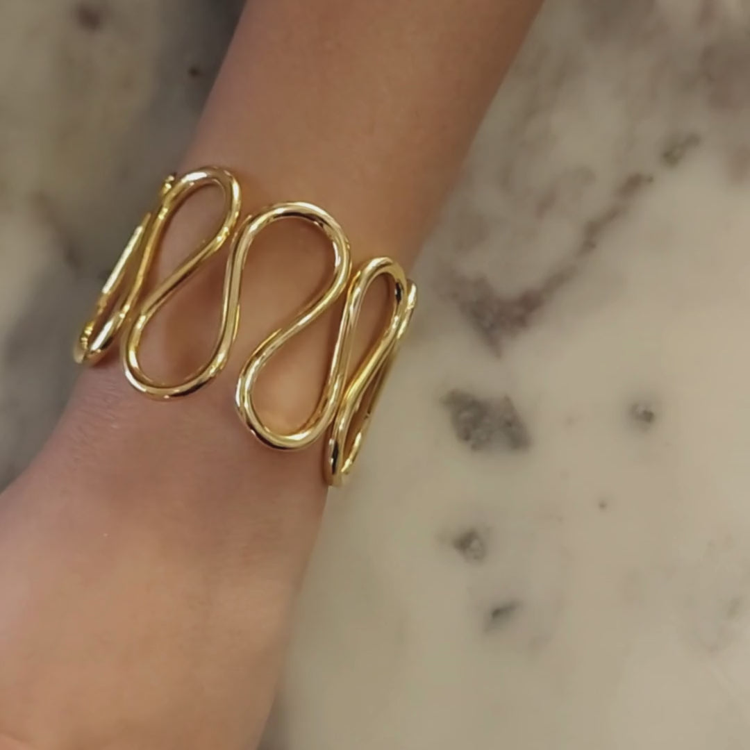 Gold-plated spiral handcuff bangle with wave-like design, crafted from brass