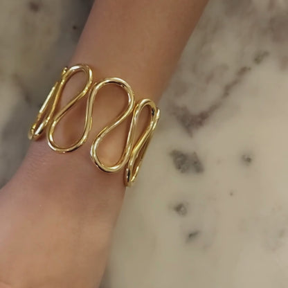 Gold-plated spiral handcuff bangle with wave-like design, crafted from brass