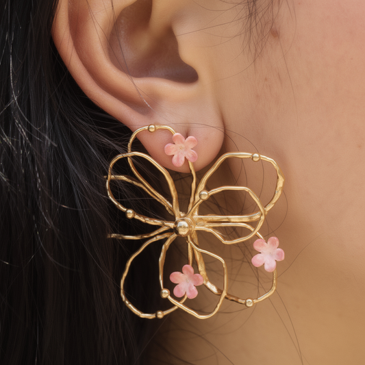 Gold floral earring with pink enamel flowers worn by a person